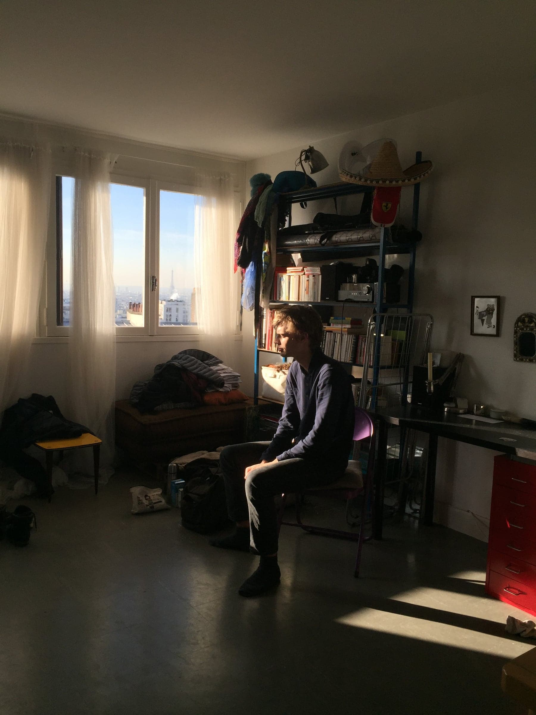 a young man sitting in a sunlit room, the eiffel tower small in the window