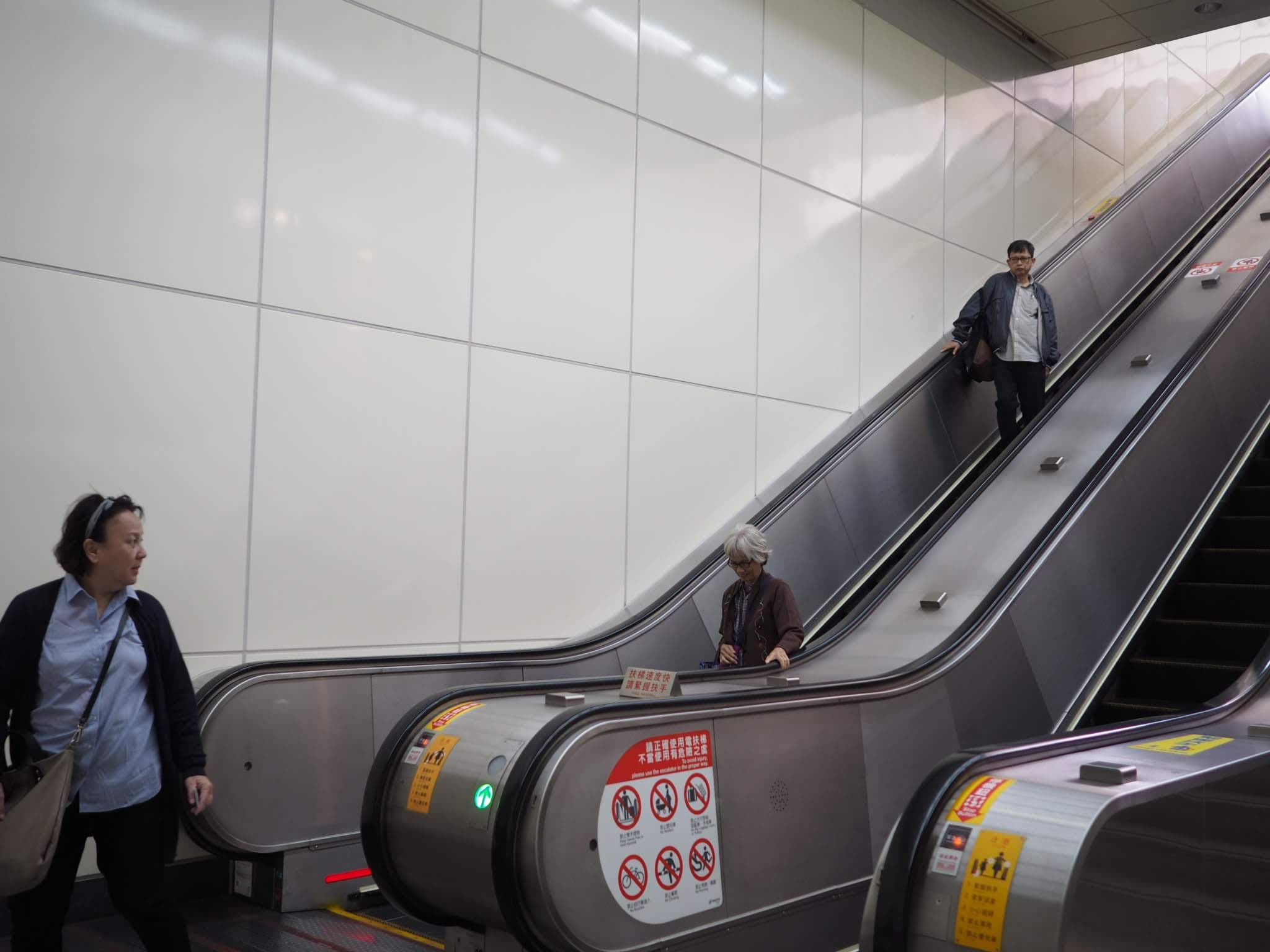 a man riding an escalator down, a woman waiting at the bottom